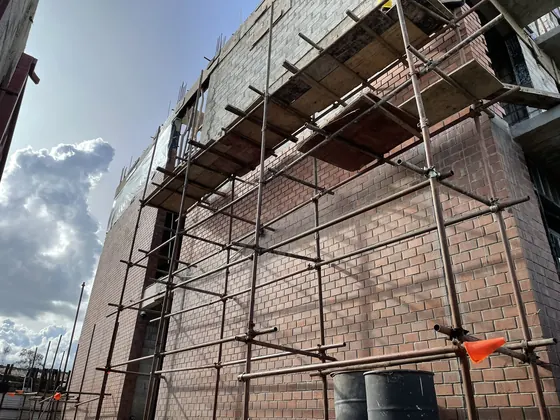 Face brick rising behind timber scaffolding on the side of the building.
