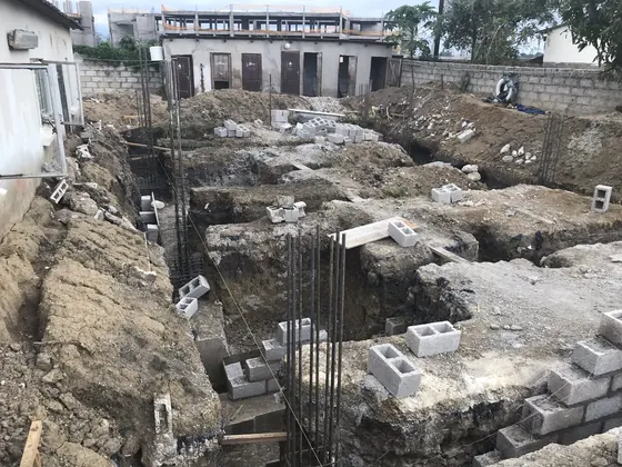 Foundation trenches and concrete block footings on a cleared site, with neighbouring houses behind.
