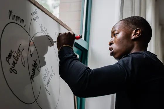 A person draws overlapping circles on a whiteboard with a red marker, working through an idea.