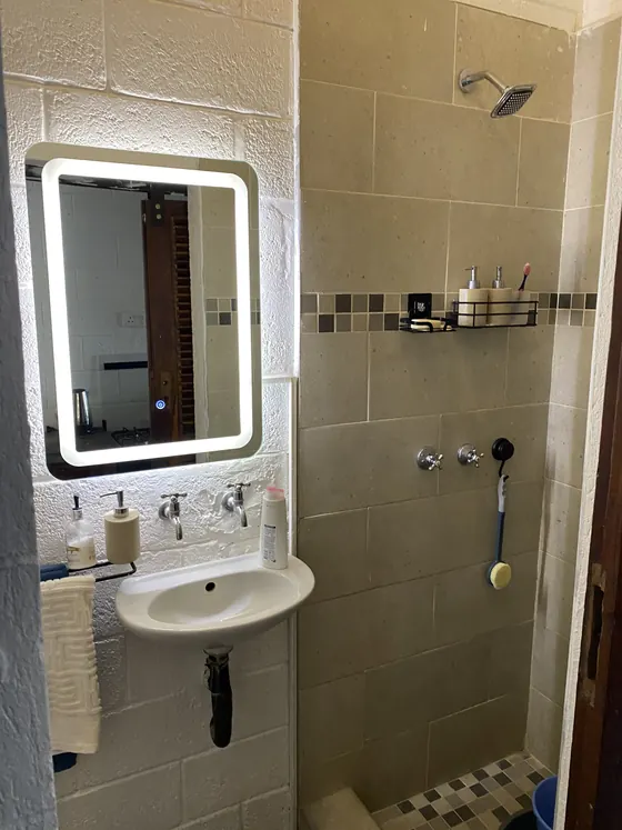 A tiled shower room with a lit round-cornered mirror above a small basin and a walk-in shower.